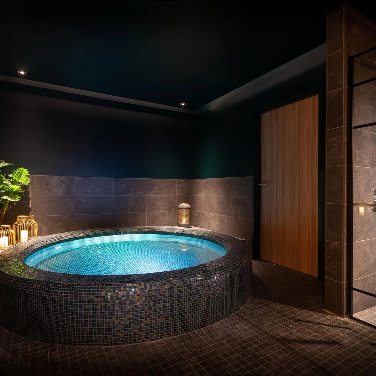 Luxurious bathroom with a large circular bathtub surrounded by mosaics, lit candles on a table, and a green plant