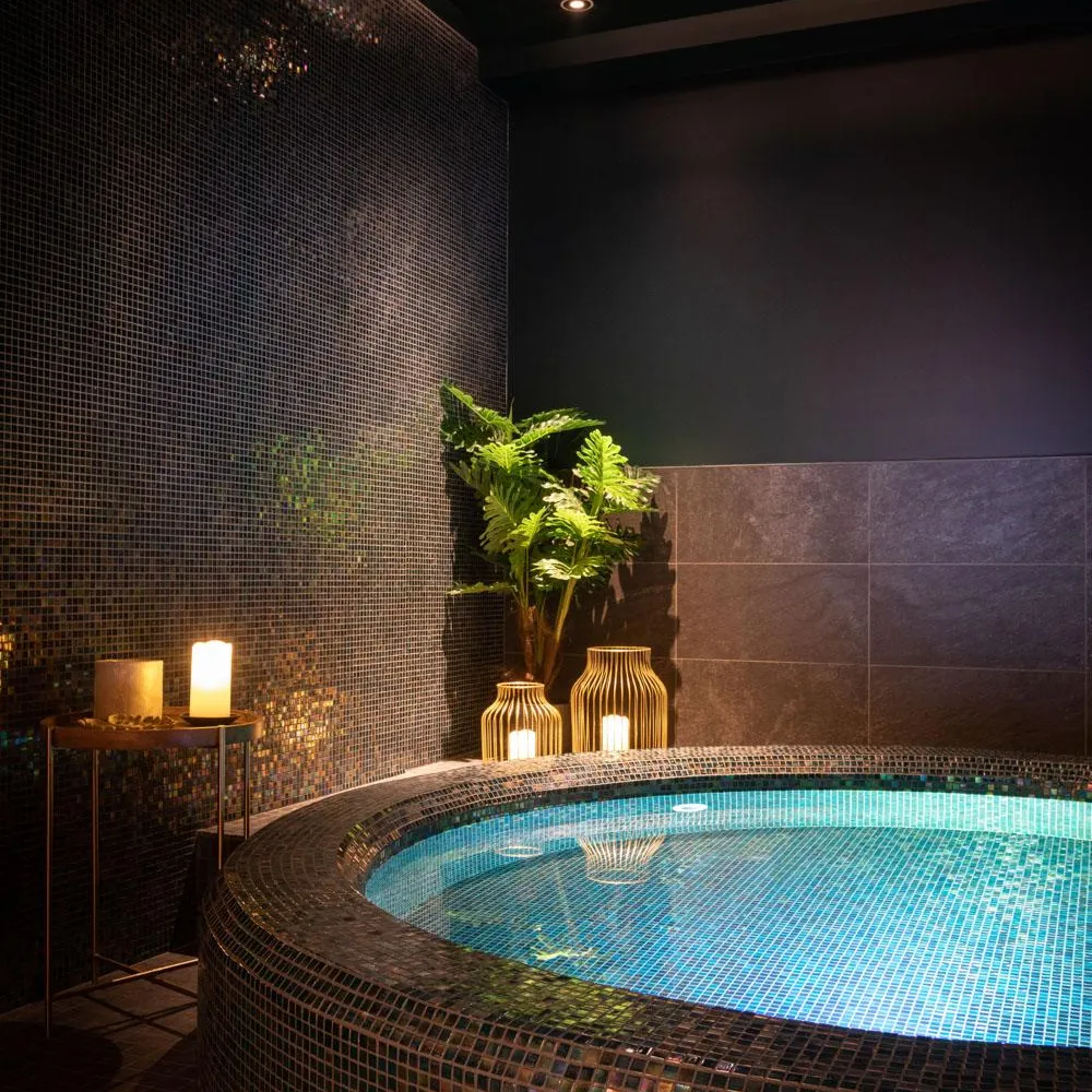 Indoor pool with blue lighting, surrounded by colorful mosaics, and decorated with plants and lanterns