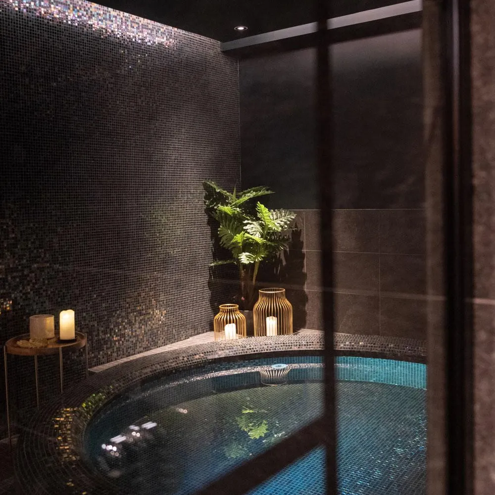 Indoor pool with blue mosaic, plants, and candles on a wall shelf