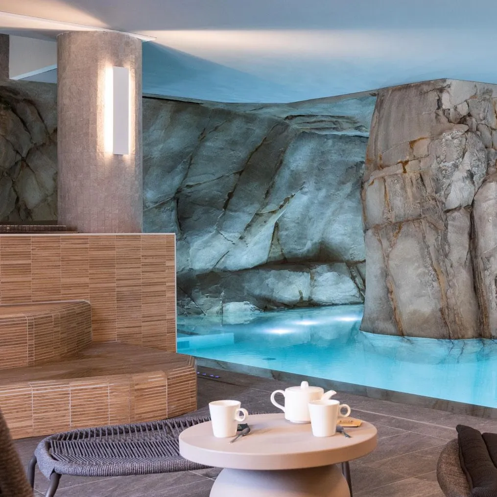Ein Wohnzimmer mit einem Couchtisch, Tassen und einer Teekanne, vor einer mit Felsmustern verzierten Wand und einem beleuchteten Pool