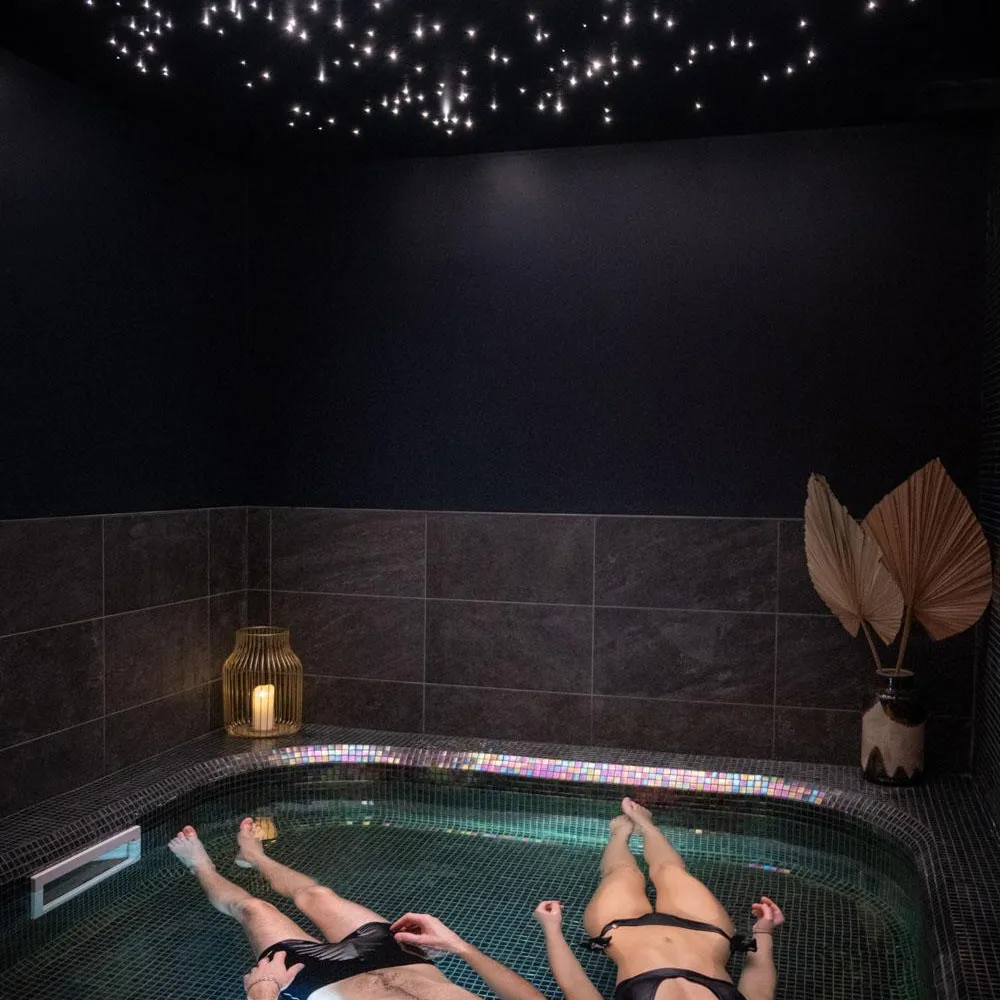 Two people lying in a hot tub with colored underwater lights, under a ceiling decorated with string lights.