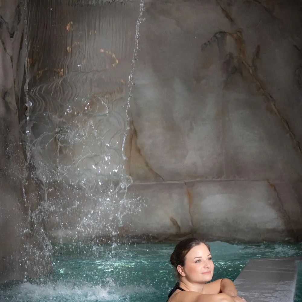 Eine Frau liegt in einem Pool, während Wasser über die Felswand hinter ihr herabfließt.