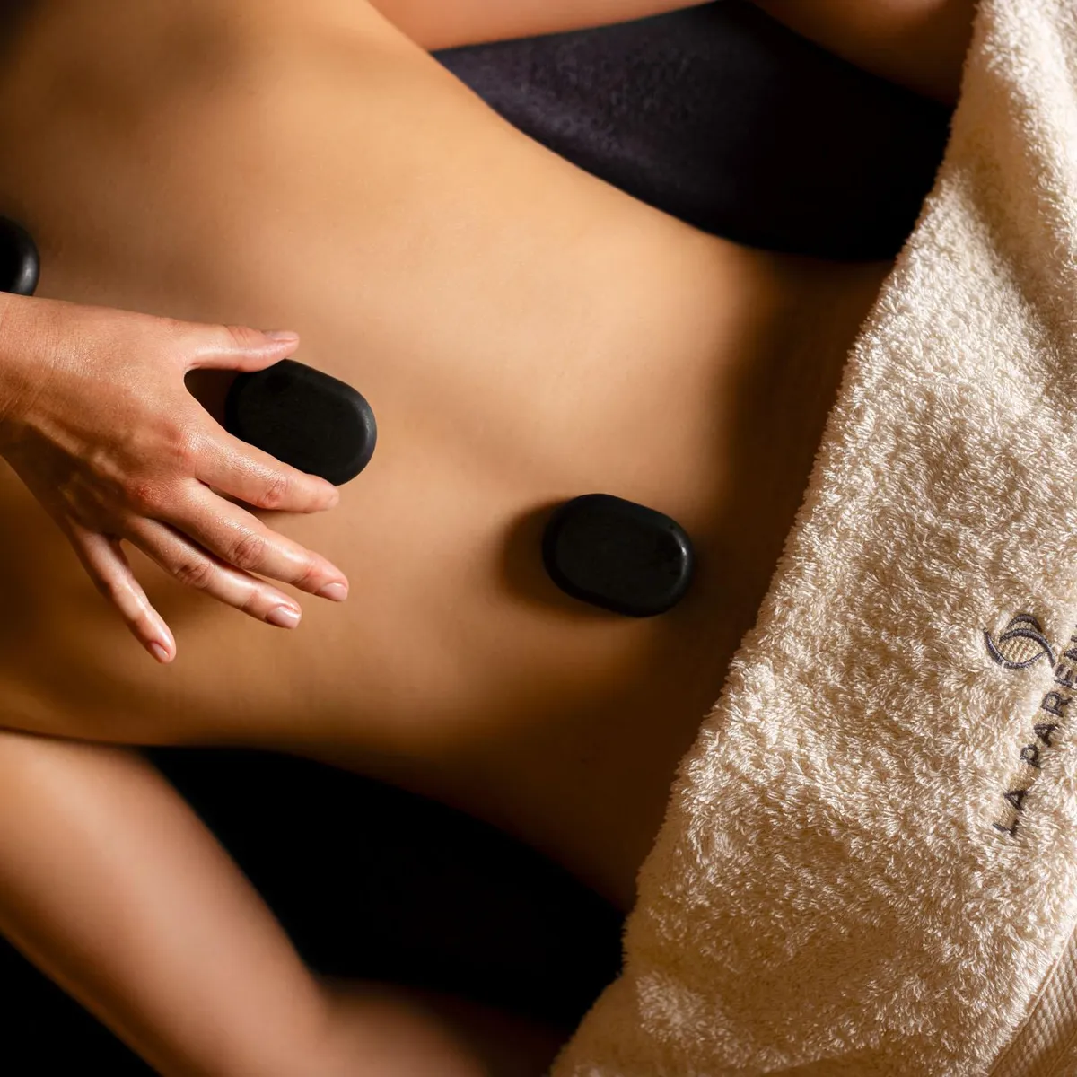 A person receives a hot stone massage on the back, partially covered with a towel.
