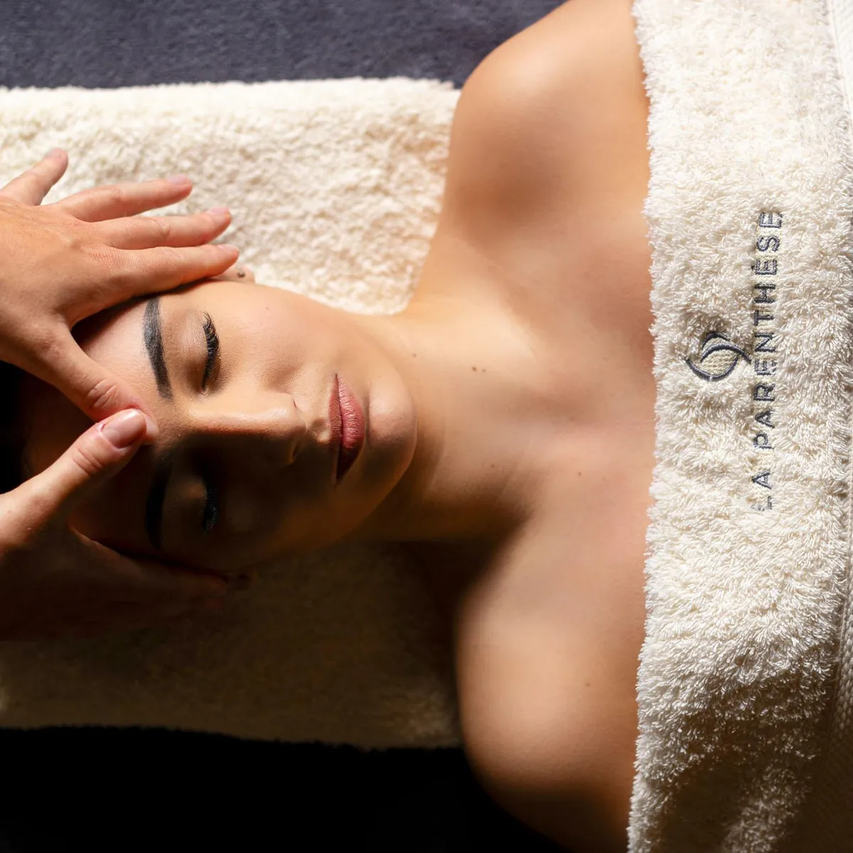 A person receives a facial massage, lying on their stomach, covered with a towel with an inscription.