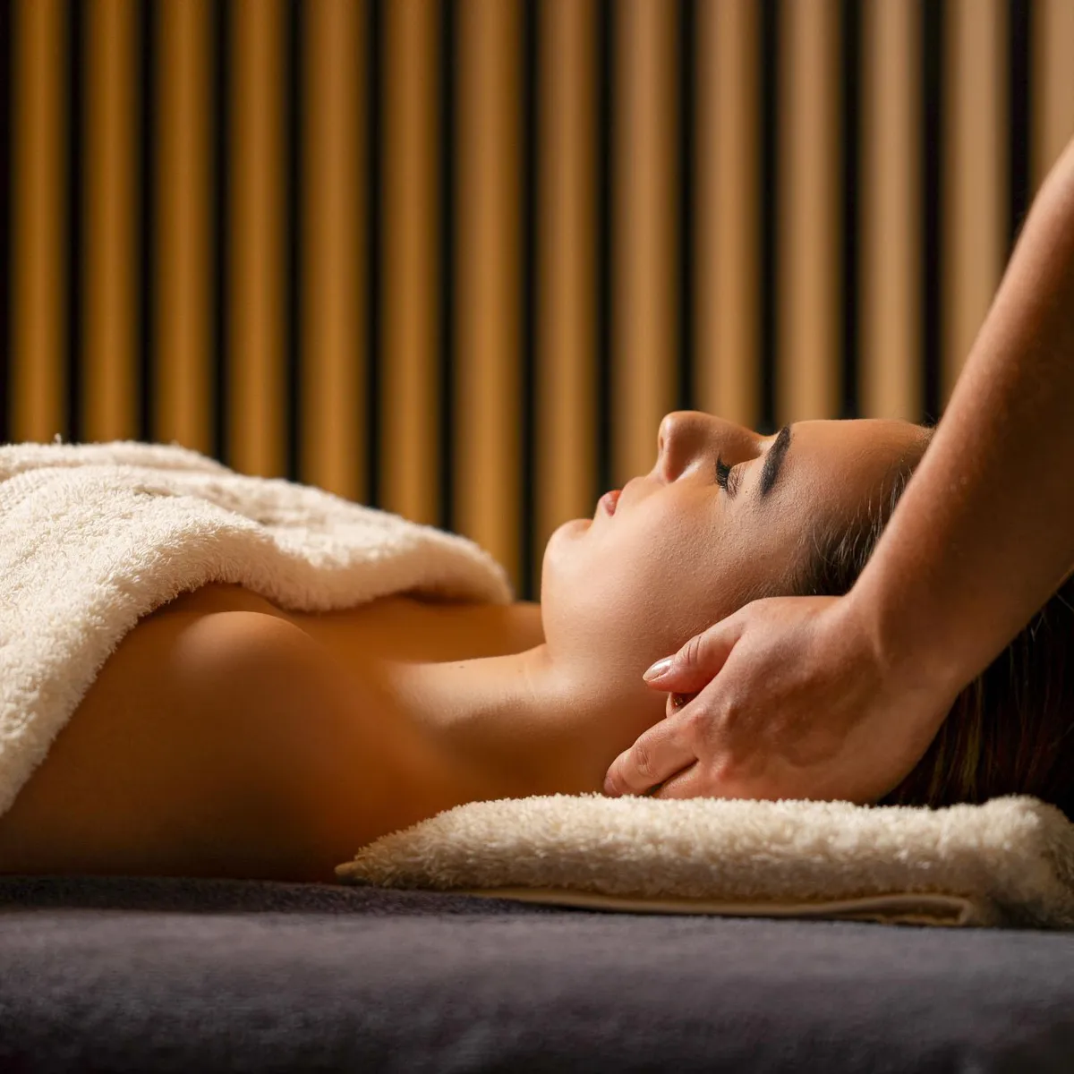 A person receives a massage on a massage bed covered with towels, in a room with vertically striped walls.
