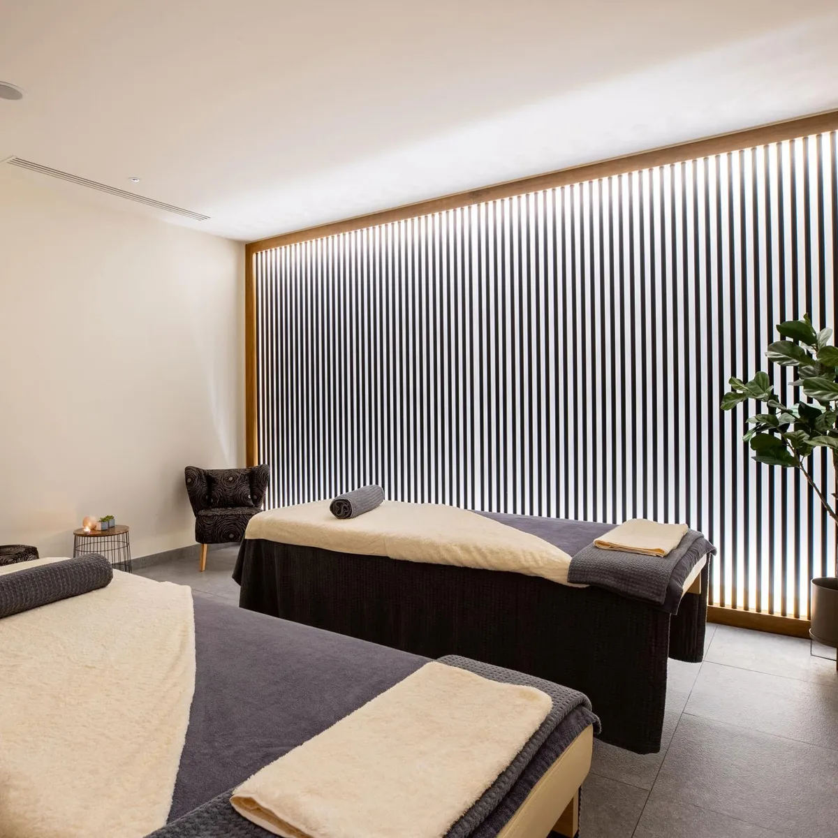 Massage room with two massage tables, towels, a plant, and candles.