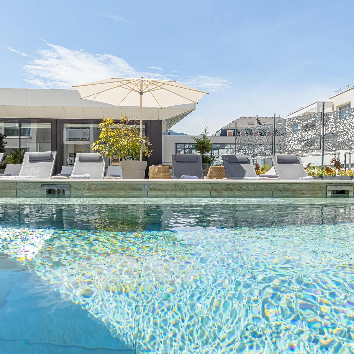 Piscine avec transats et parasols devant un bâtiment moderne aux balcons métalliques