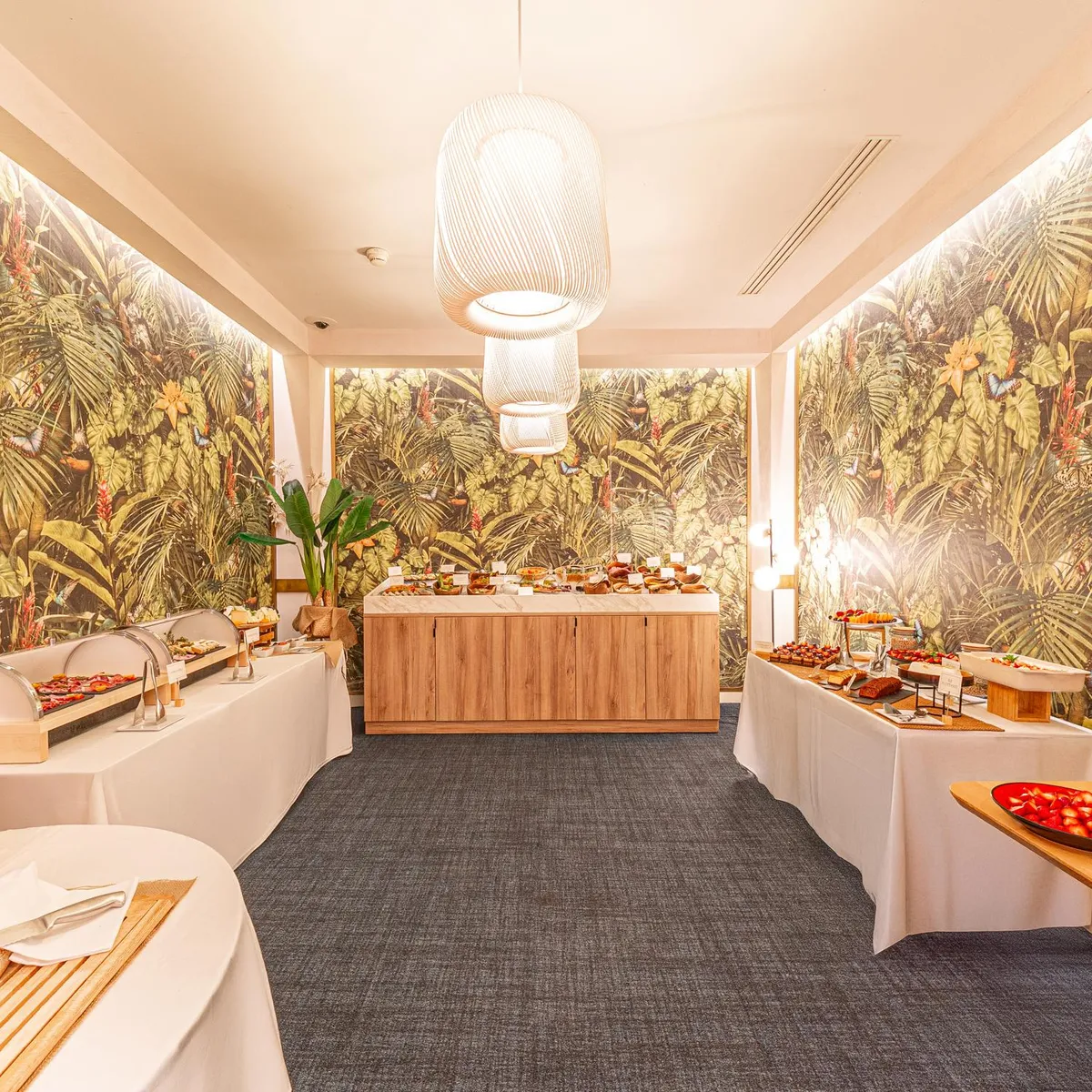 Buffet with various dishes arranged on tables covered with white tablecloths, in a room decorated with walls depicting a tropical jungle