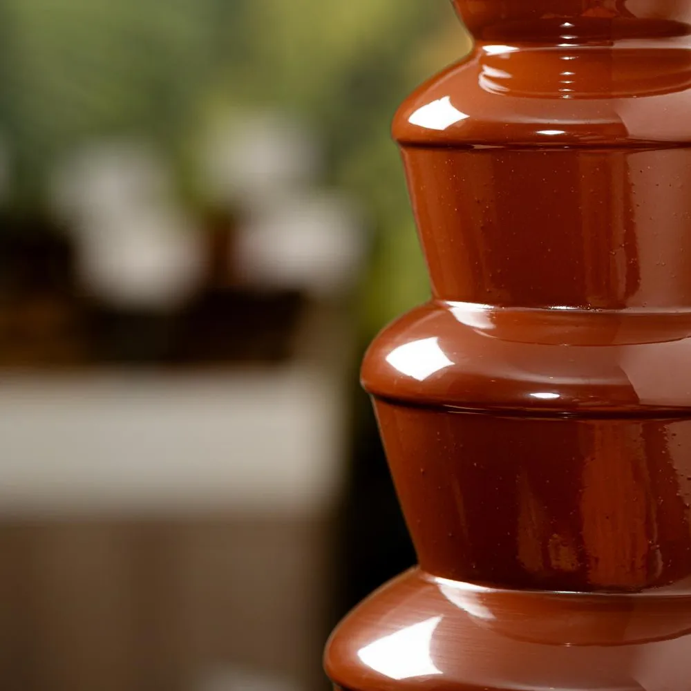 A red multi-tiered ceramic pot is placed outside against a blurred background of greenery and stone structures.