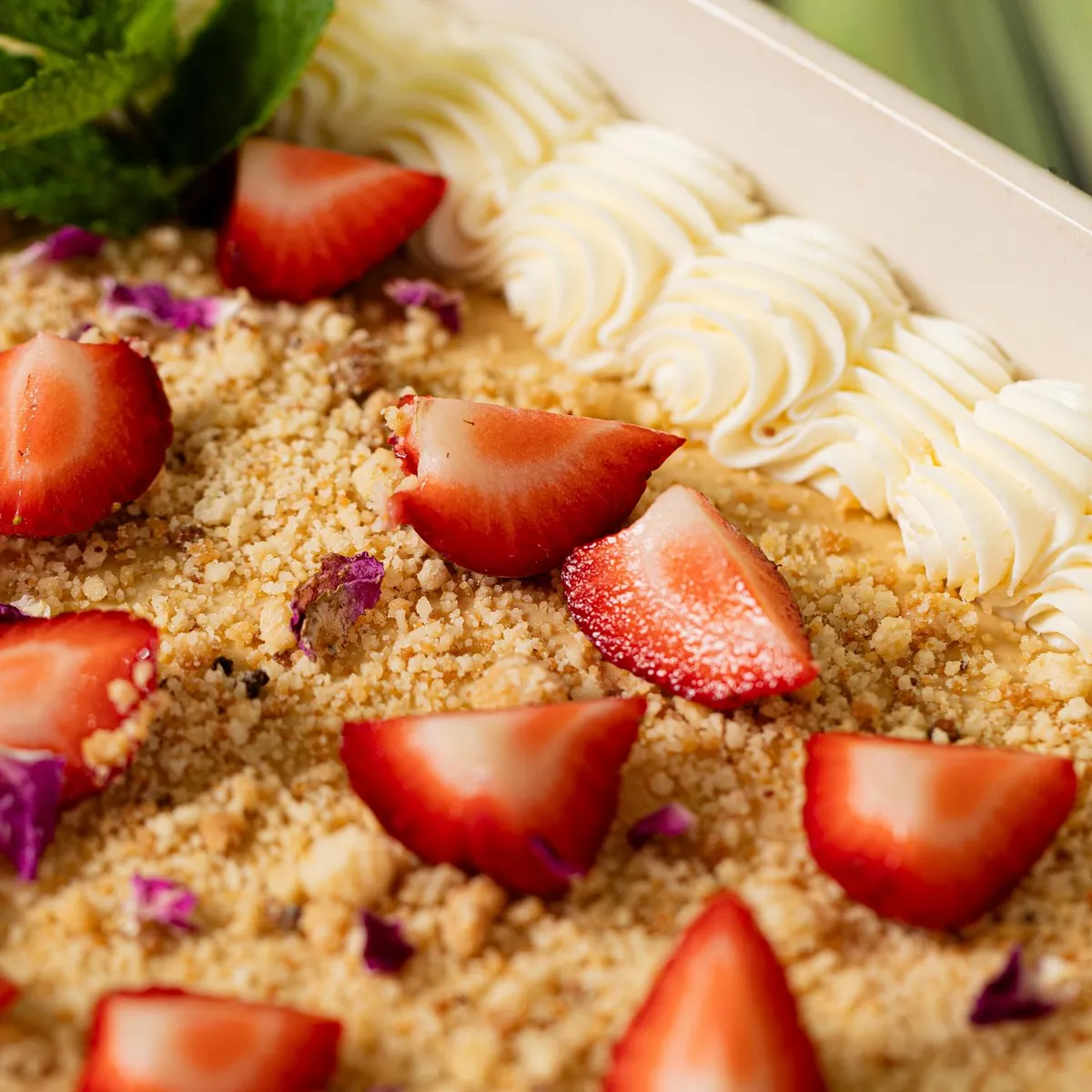 A dish containing strawberry slices, quinoa seeds, and a white cream topping, accompanied by celery stalks in the background.
