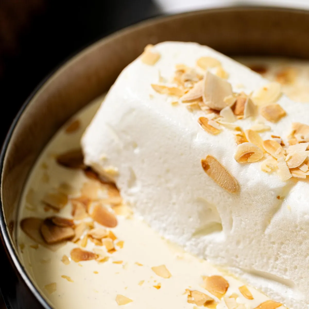 A portion of white dessert topped with almond shavings in a black dish