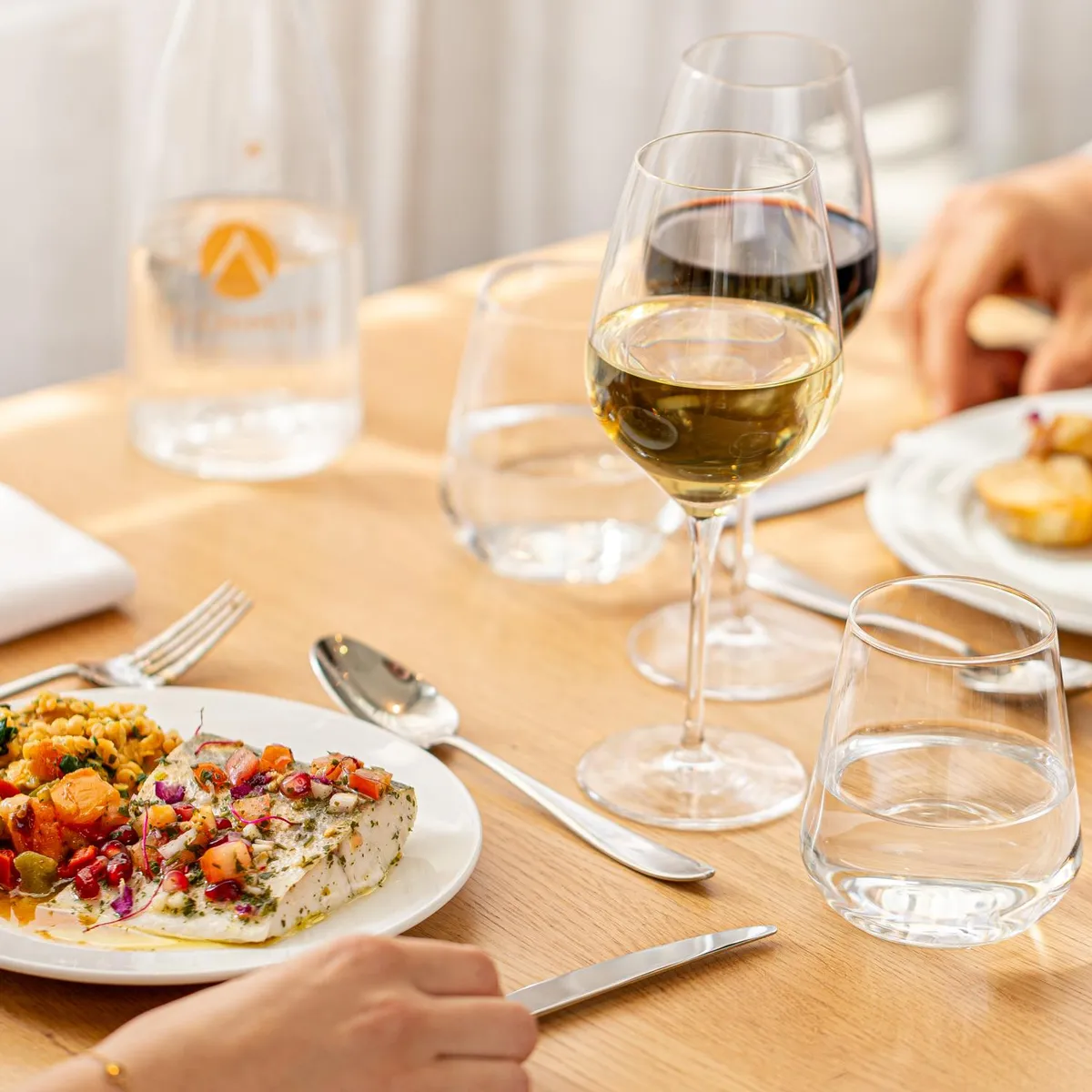 People are sitting at a table and eating various dishes accompanied by wine and water.