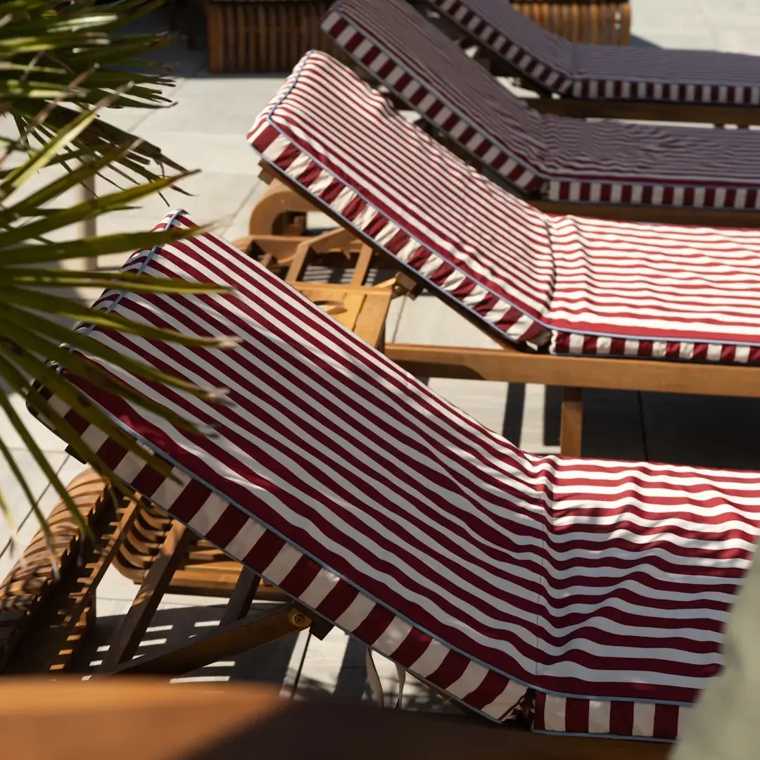 Des transats en bois avec des coussins rayés rouges et blancs sont disposés sur une terrasse en béton près d'une plante verte