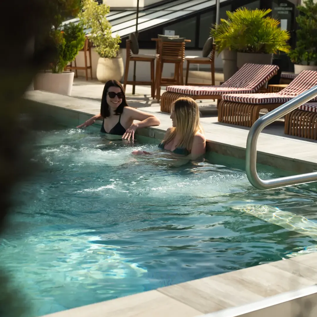Deux personnes nagent dans une piscine avec des chaises longues et des tables à proximité