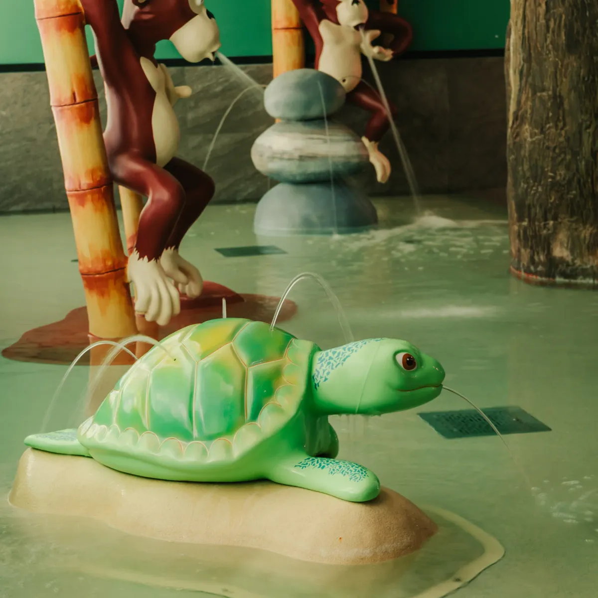 Deux singes et une tortue en plastique dans une aire de jeux aquatique avec des jets d'eau