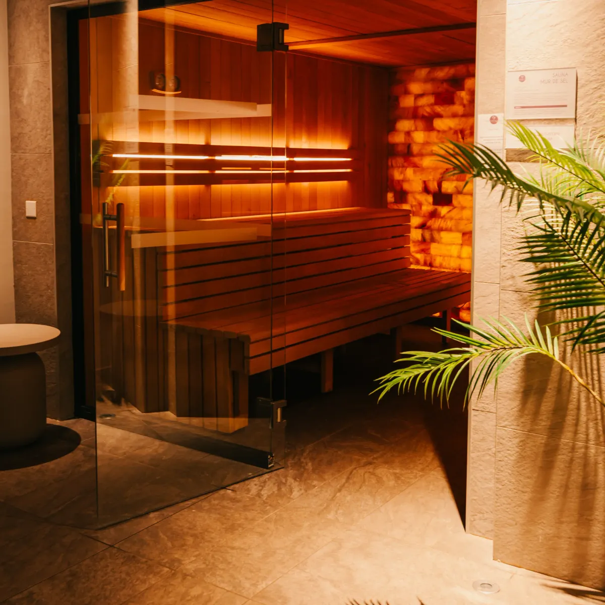 Salle de sauna en bois avec des bancs superposés, éclairée par des lumières chaudes, vue depuis l'entrée ouverte