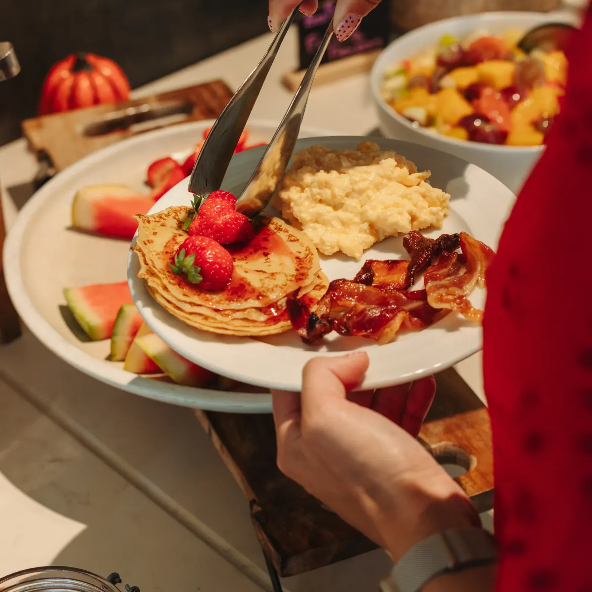 Une personne sert des pancakes garnis de fraises, de bacon et de purée de patate douce sur une assiette