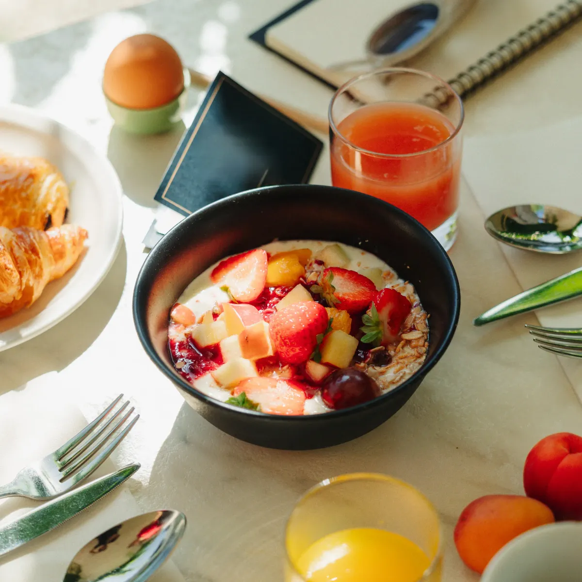 Un bol de porridge aux fruits frais, des croissants, des verres de jus, des œufs et des couverts sur une table