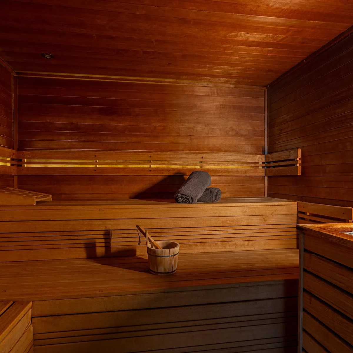 Wooden sauna interior with benches, a wooden bucket, and hot stones