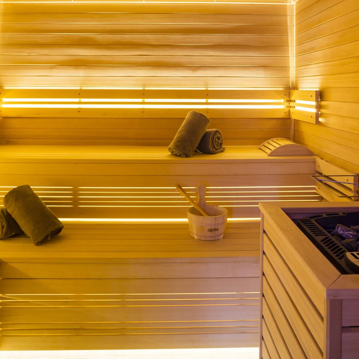 Wooden sauna room with benches, wooden bucket and ladle, and heated stones on a stove