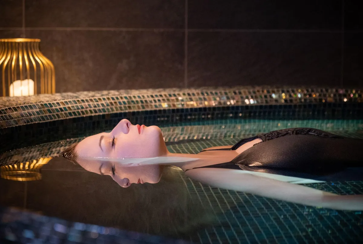 Une personne allongée dans une piscine d'eau avec des lumières sous-marines et une lampe à l'arrière-plan