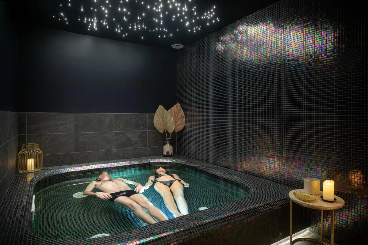 Two people lying in a hot tub, surrounded by colorful mosaics and candles, with a starry ceiling.