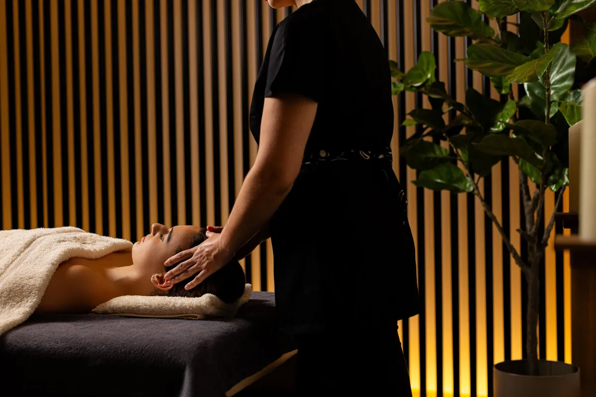 Eine Person erhält eine Kopfmassage, während sie auf einer Massageliege liegt, während eine andere Person die Massage durchführt.
