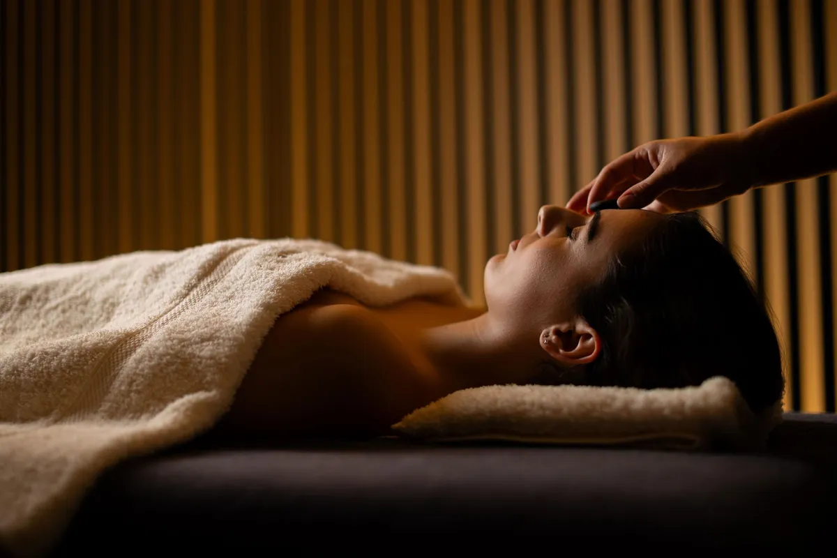 Eine Person, die auf einem Handtuch liegt, erhält eine Gesichtsmassage in einem Raum mit geriffelten Wänden.