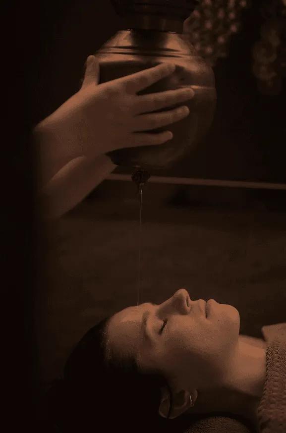 Eine Person erhält einen Wasserstrahl auf die Stirn aus einem von einer Hand gehaltenen Behälter.