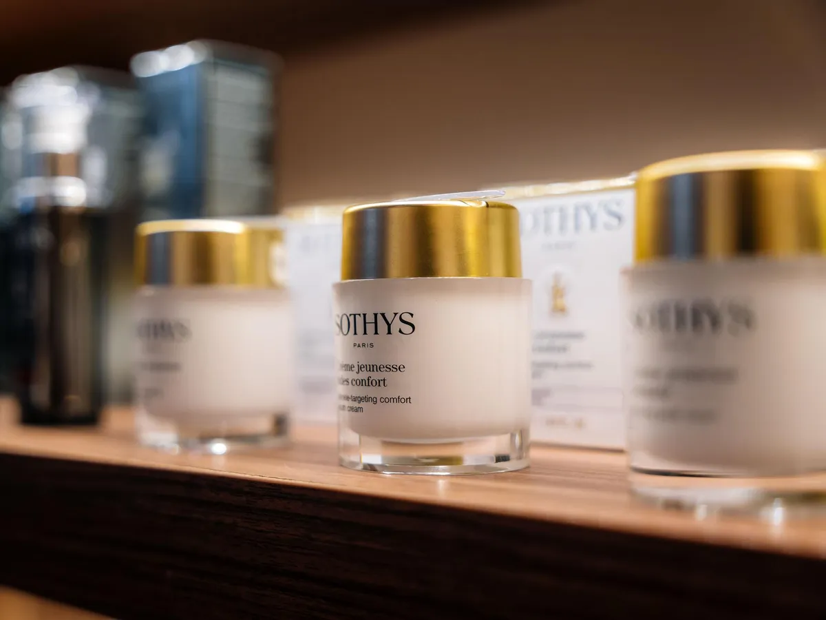 Mehrere Sothys Paris Kosmetikcreme-Gläser mit goldenen Deckeln auf einem Holzregal
