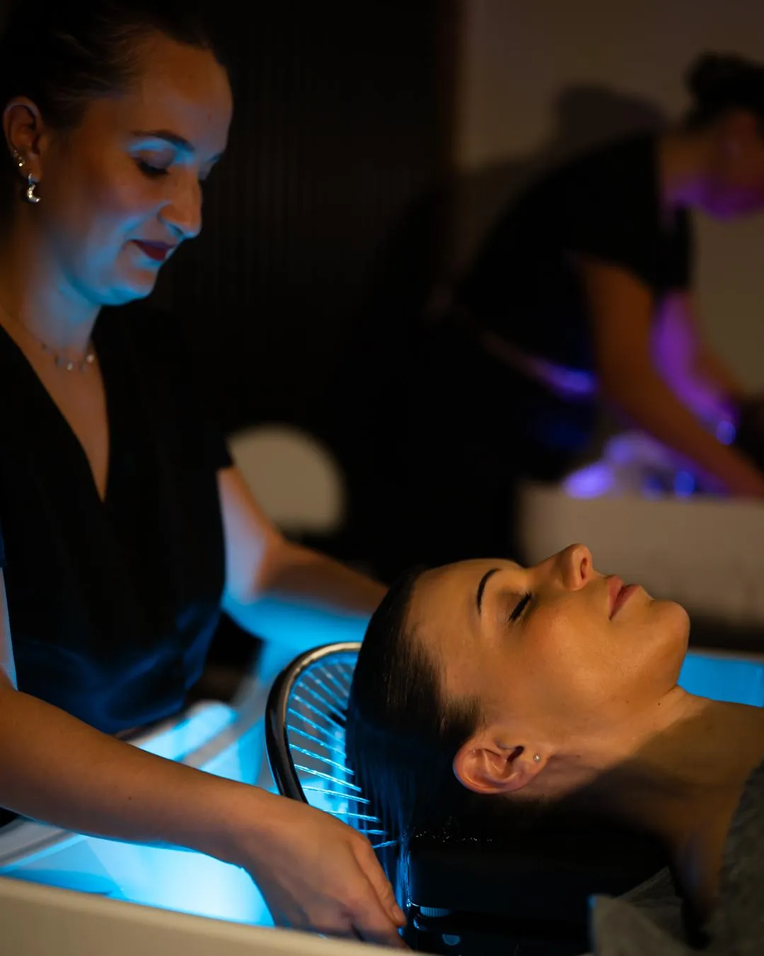Eine Frau erhält eine Gesichtsbehandlung in einem Schönheitssalon, während sie unter blauem Licht liegt.