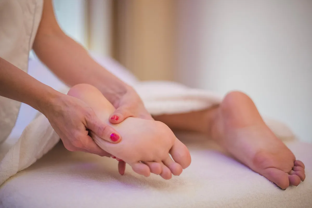 A person receives a foot massage from another person; the feet have toenails painted in different colors.