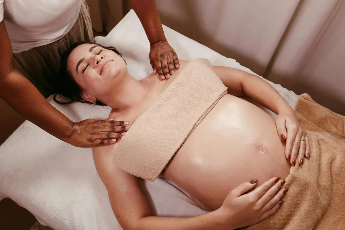 Eine liegende Person erhält eine Bauchmassage von zwei Händen, umgeben von Handtüchern.