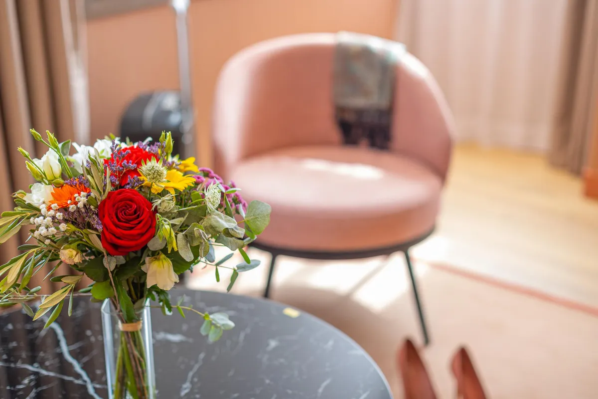 A bouquet of colorful flowers in a transparent vase placed on a black table with chairs in the background