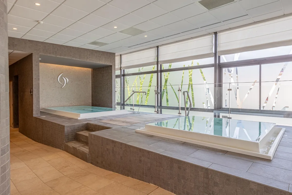 Spa-Bereich mit zwei Warmwasserbecken und einer großen Glasfront, die den Blick auf eine Außenstruktur freigibt