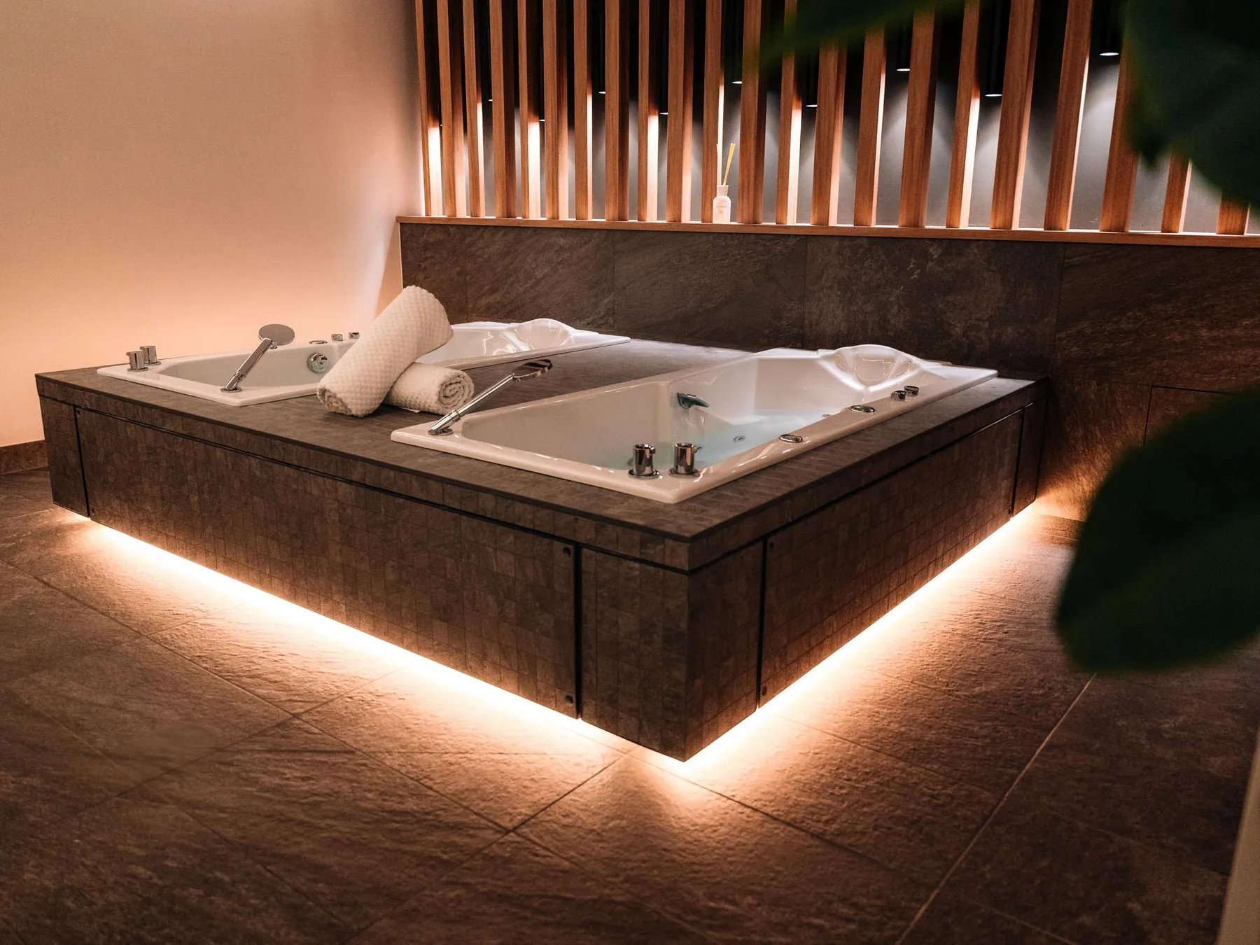 Built-in whirlpool bathtub in a stone cabinet with LED floor lighting and white towels placed on the edge