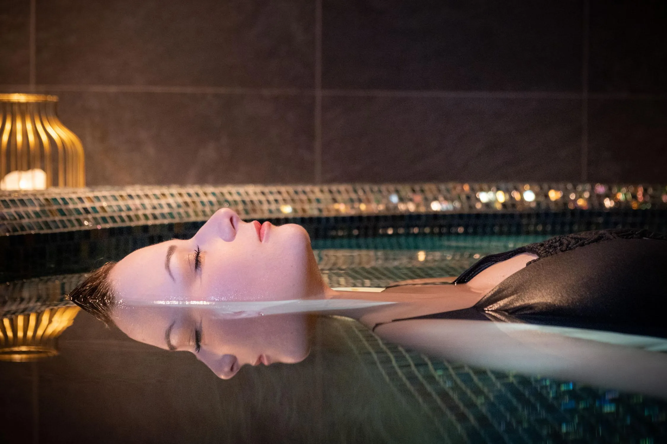 A person lying on their back in a pool with a nighttime city view in the background.