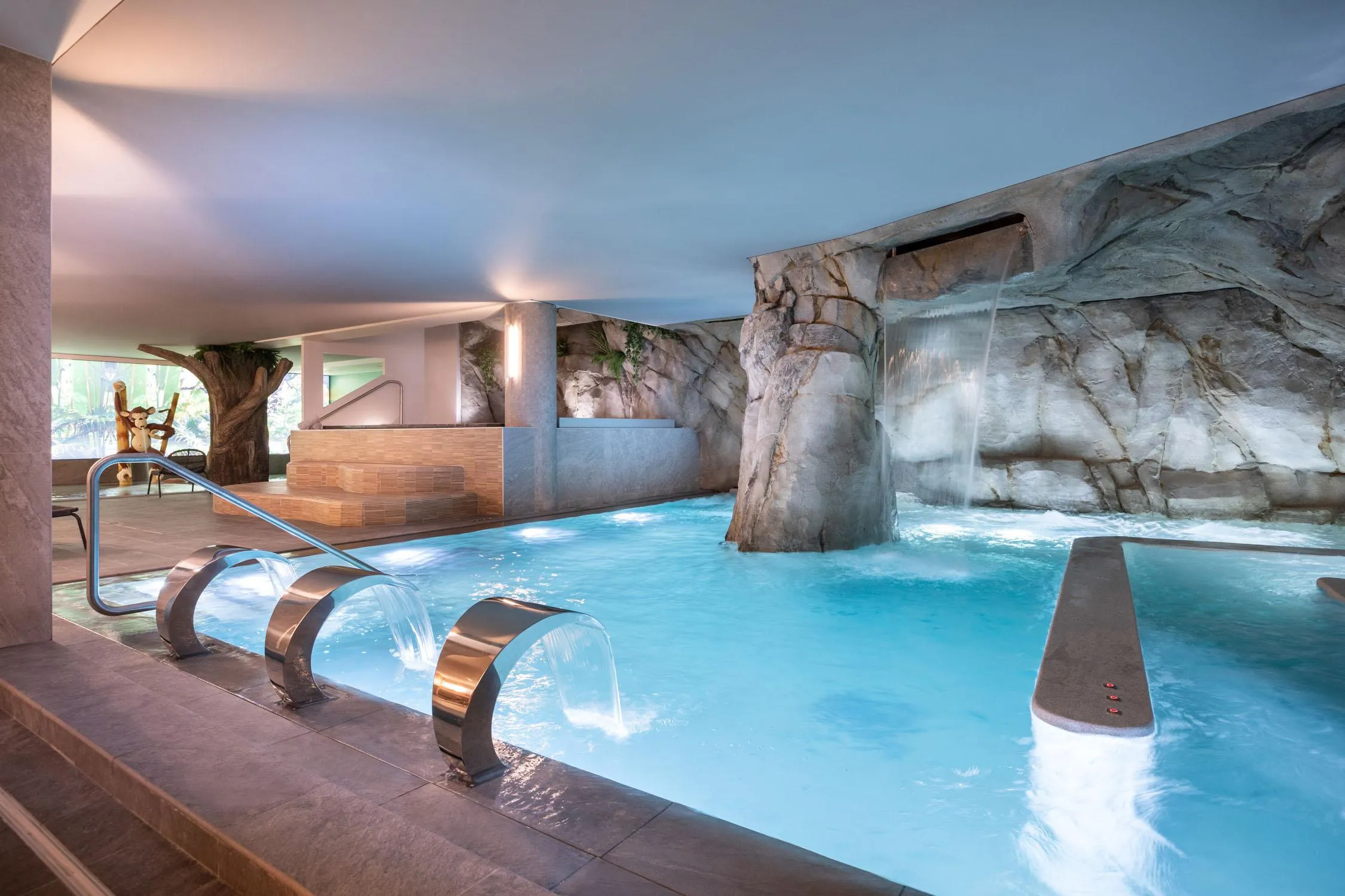 Innenpool mit Wasserfällen und künstlichen Felsen, beleuchtet durch natürliches und künstliches Licht