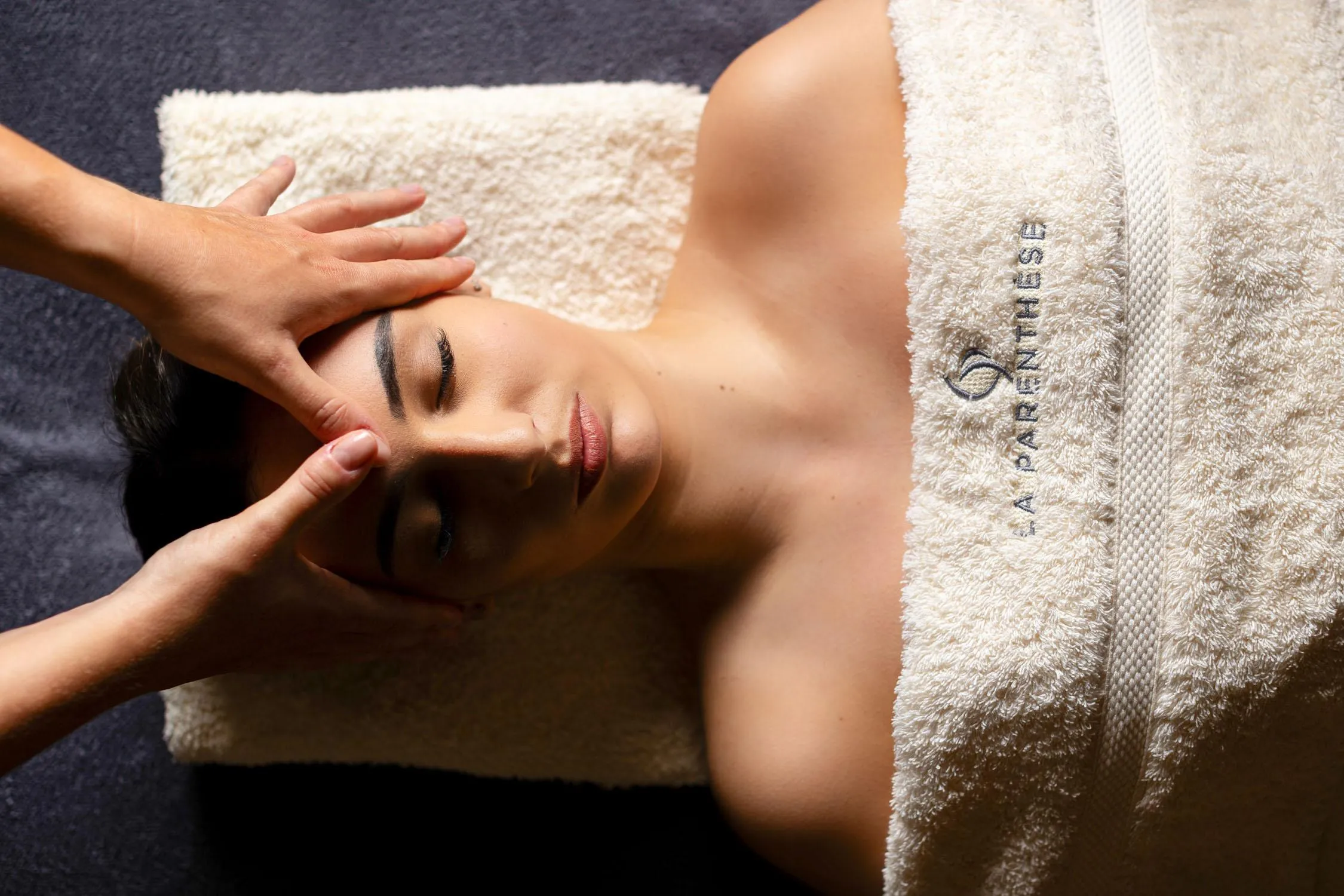Eine Person erhält eine Gesichtsmassage, liegt auf dem Bauch und ist mit einem Handtuch mit einer Aufschrift bedeckt.