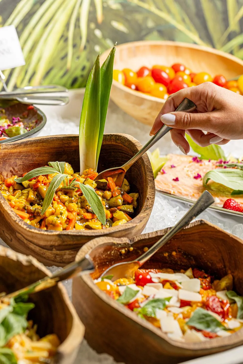 A person serves a vegetable-based dish in a wooden bowl, surrounded by similar dishes.