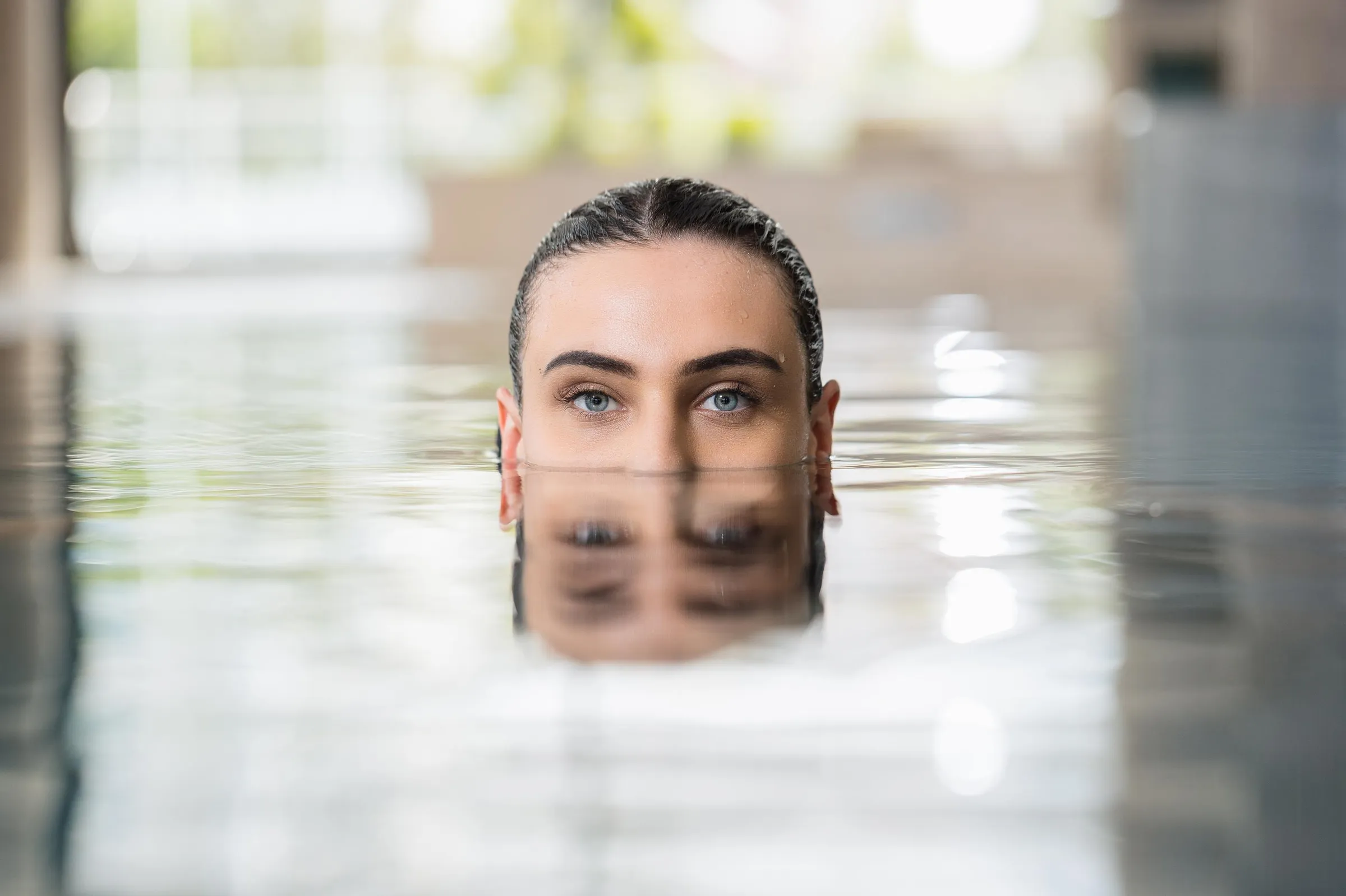 A person with tied-up hair emerges from the water in an indoor pool.