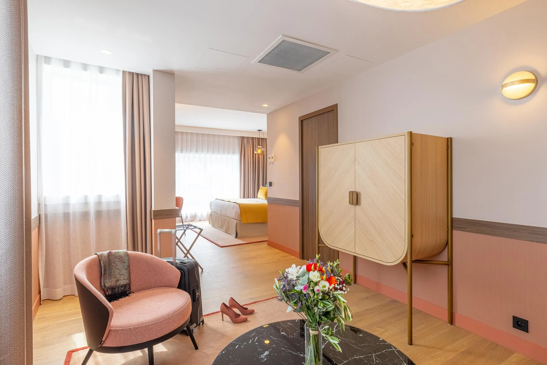 Hotelzimmer mit einem Sessel, einem Couchtisch, einer Vase mit Blumen, einem Bett und einem Kleiderschrank