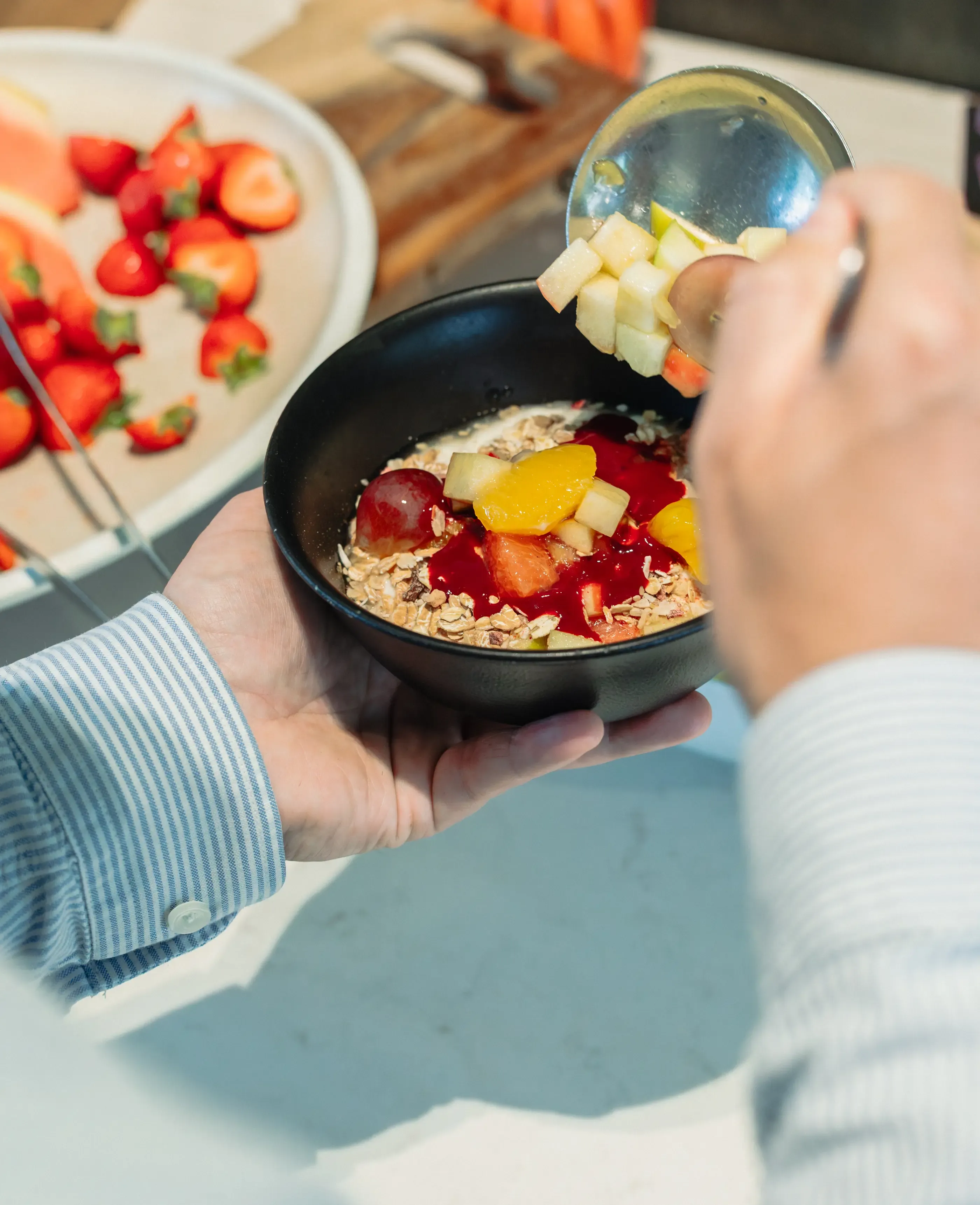 Une personne ajoute des morceaux de pomme dans un bol de muesli avec des fruits et du yaourt