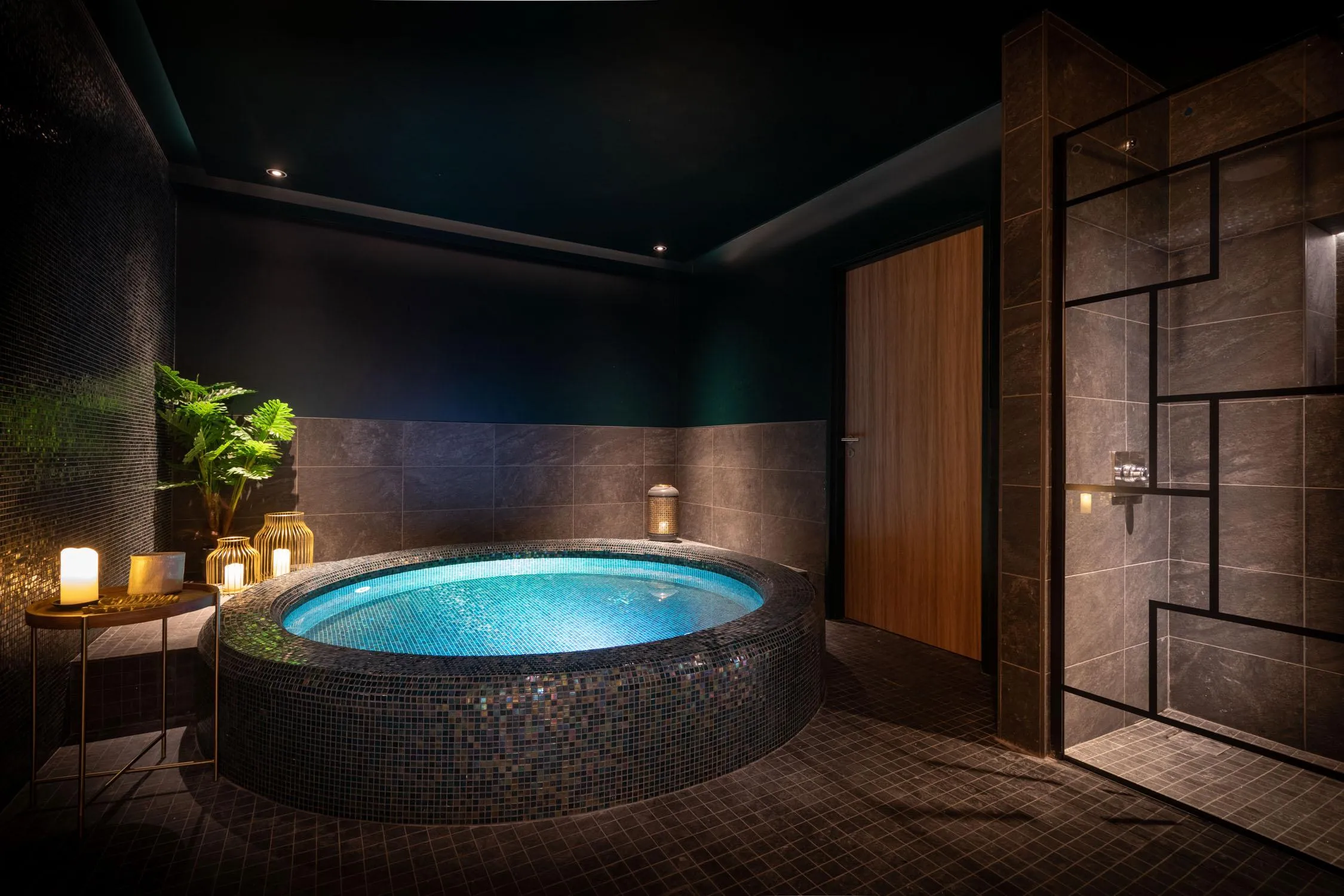 Luxurious bathroom with a large circular bathtub surrounded by mosaics, lit candles on a table, and a green plant