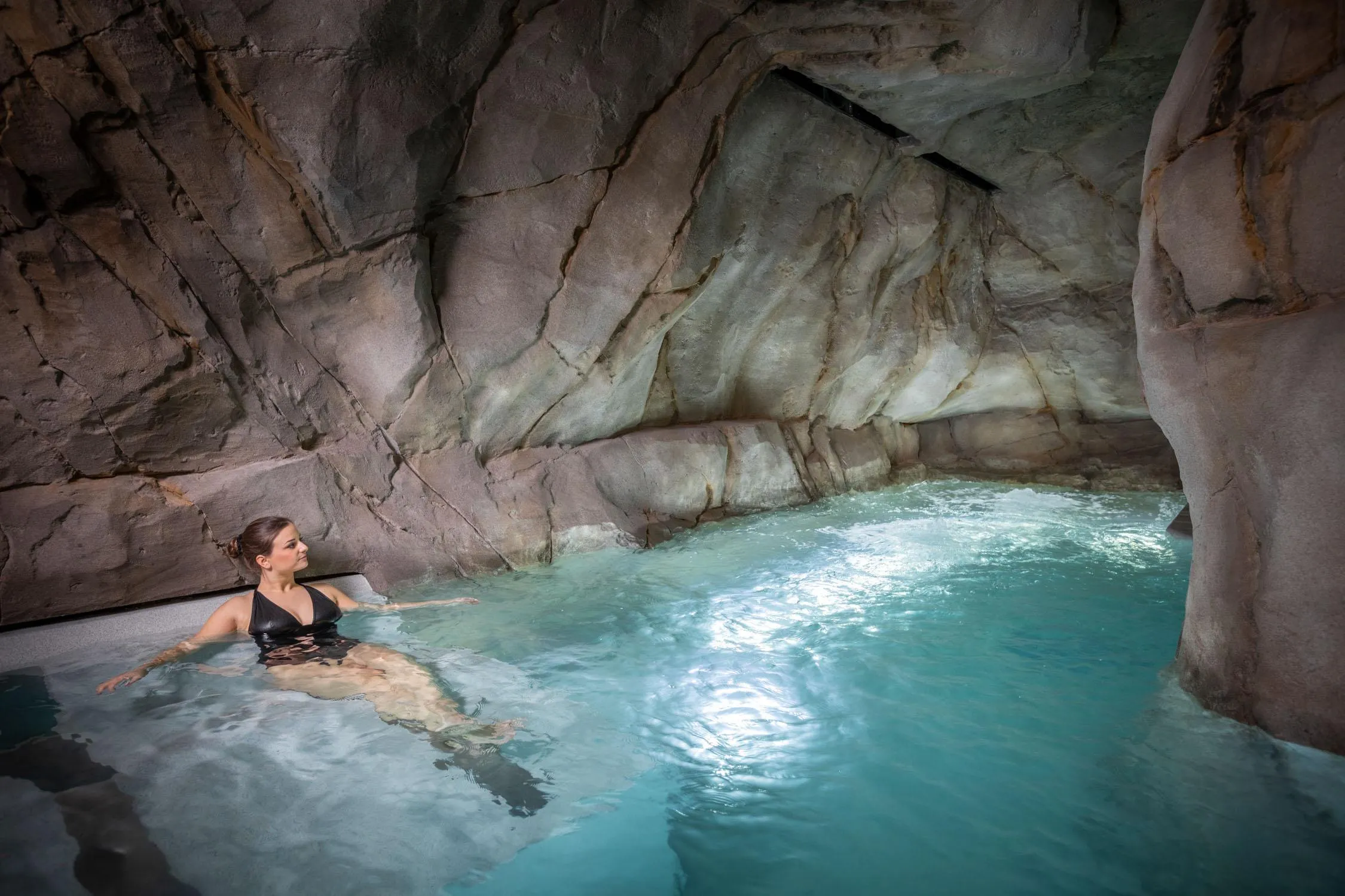 A person is swimming in a natural pool surrounded by rocks.