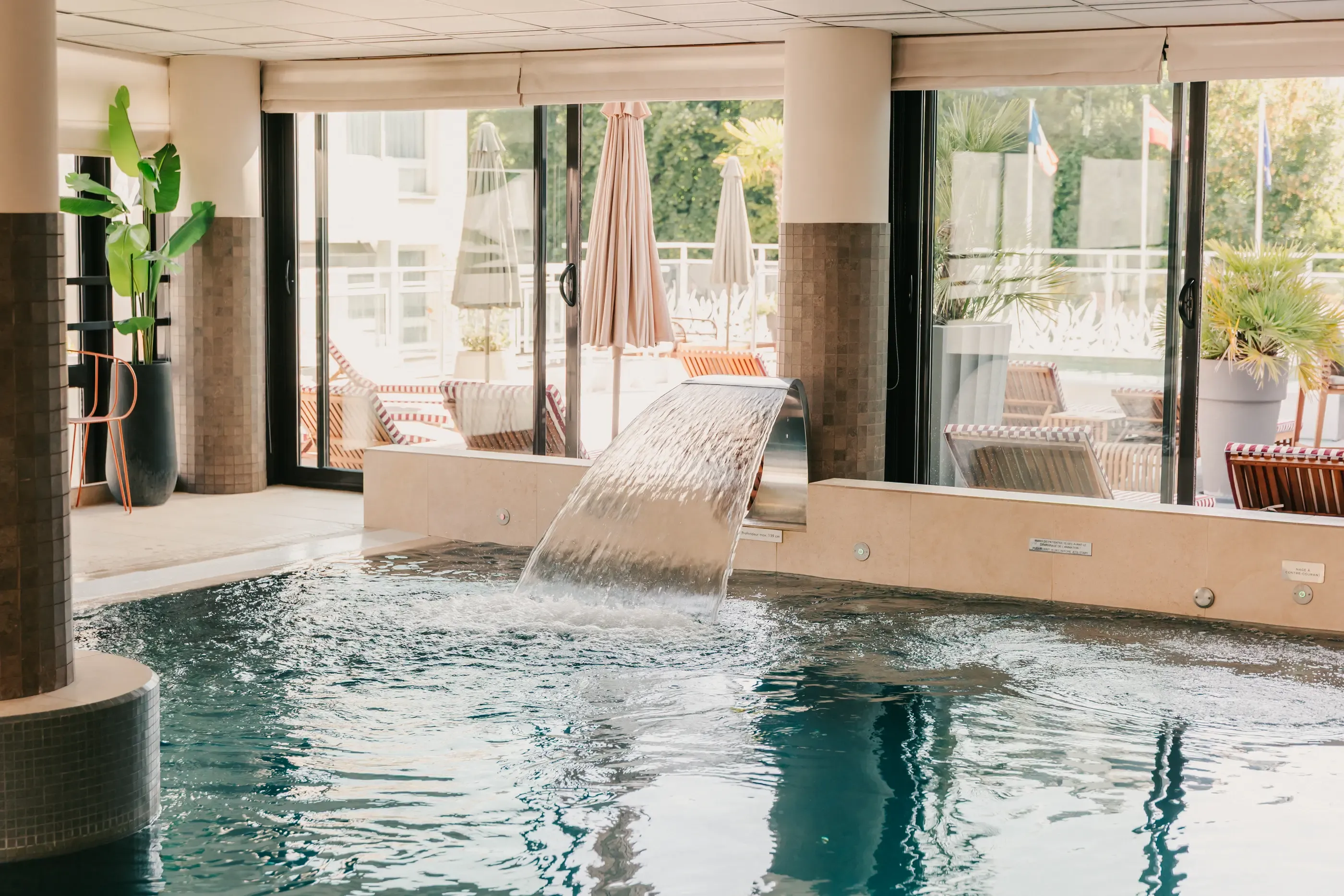 Piscine intérieure avec une cascade d'eau et une terrasse extérieure visible à travers de grandes baies vitrées