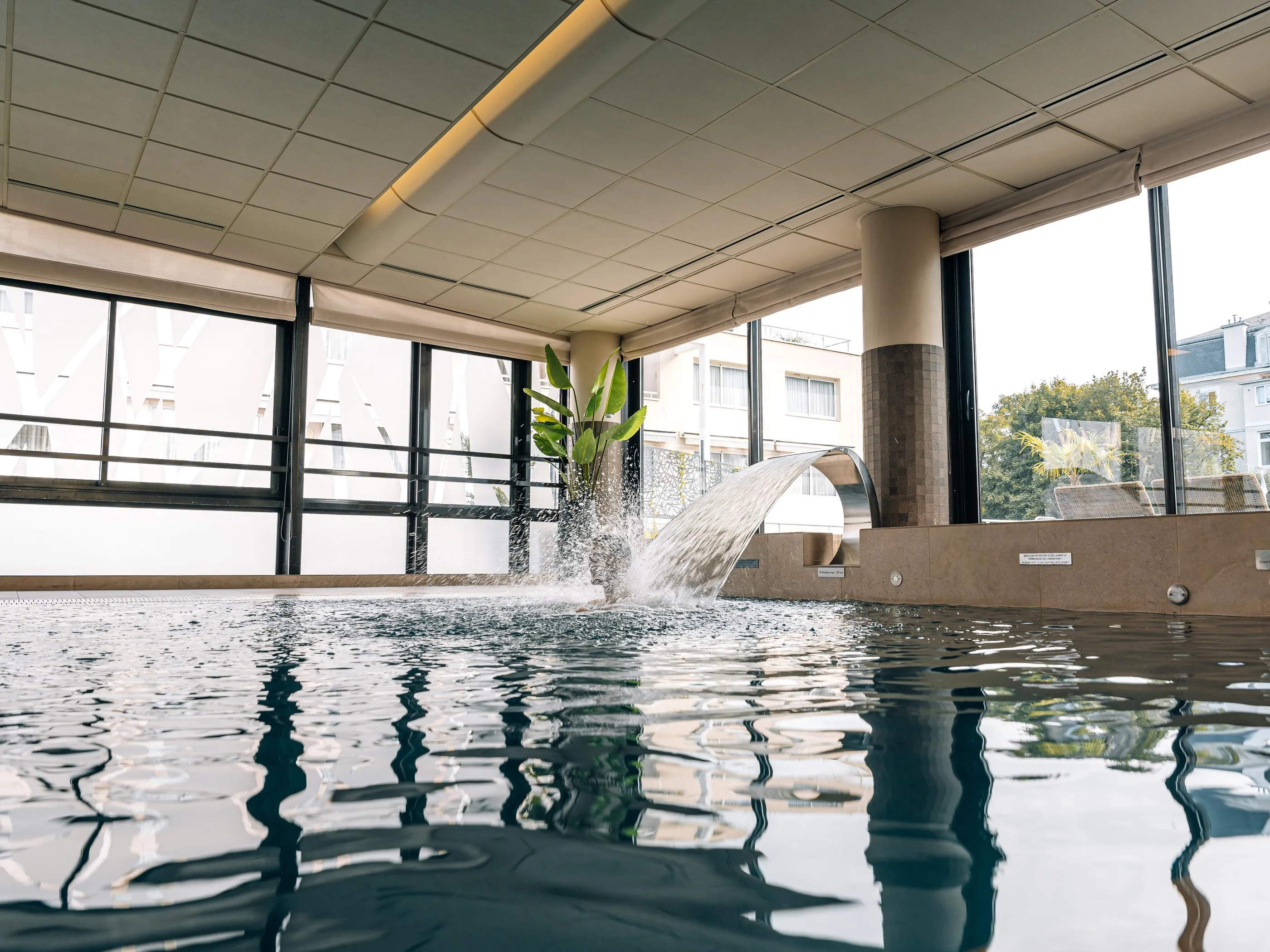 Indoor pool with a water fountain and windows overlooking an exterior building
